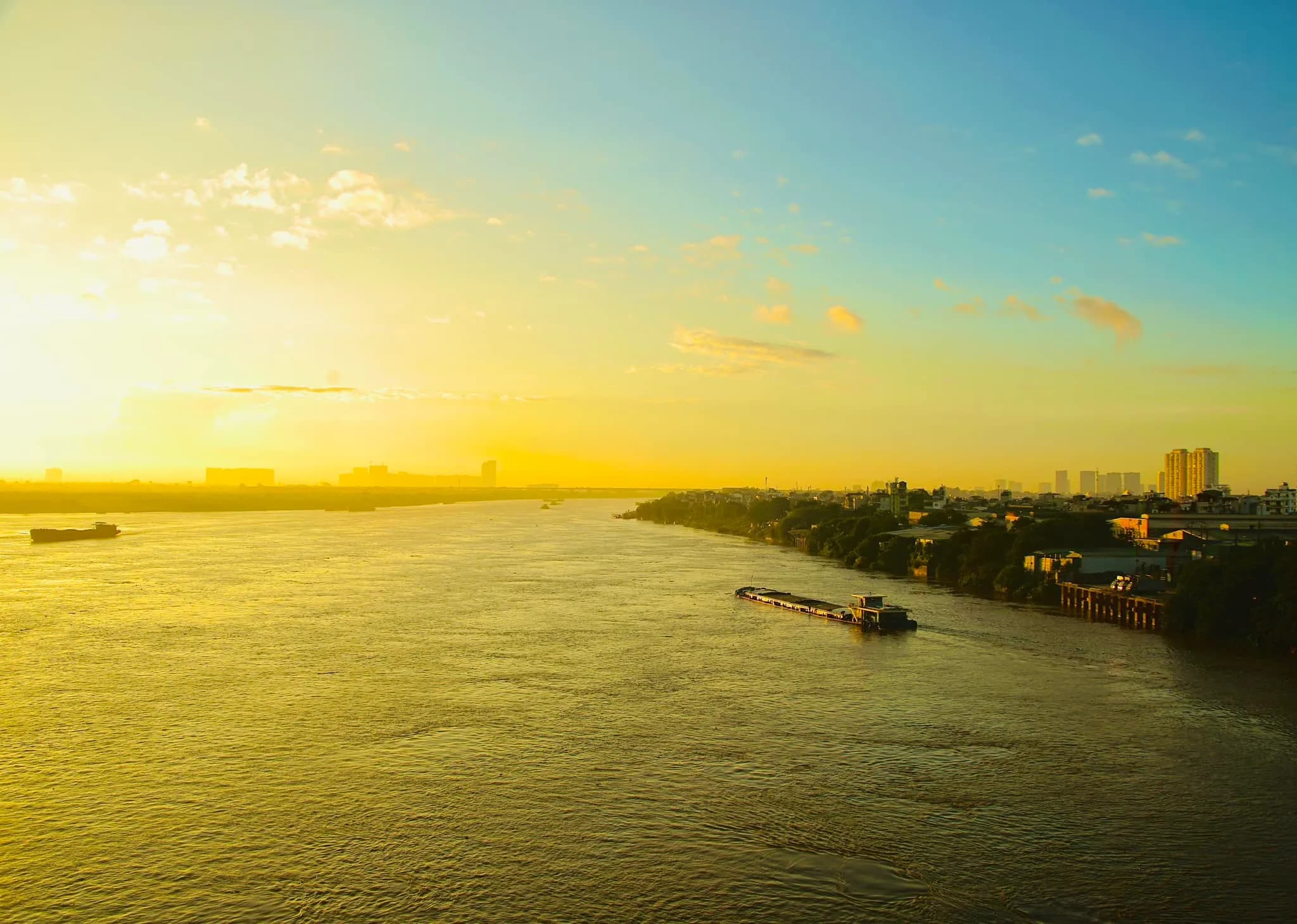 The Red River in Hanoi bathed in golden sunset light during autumn, creating a serene and picturesque landscape