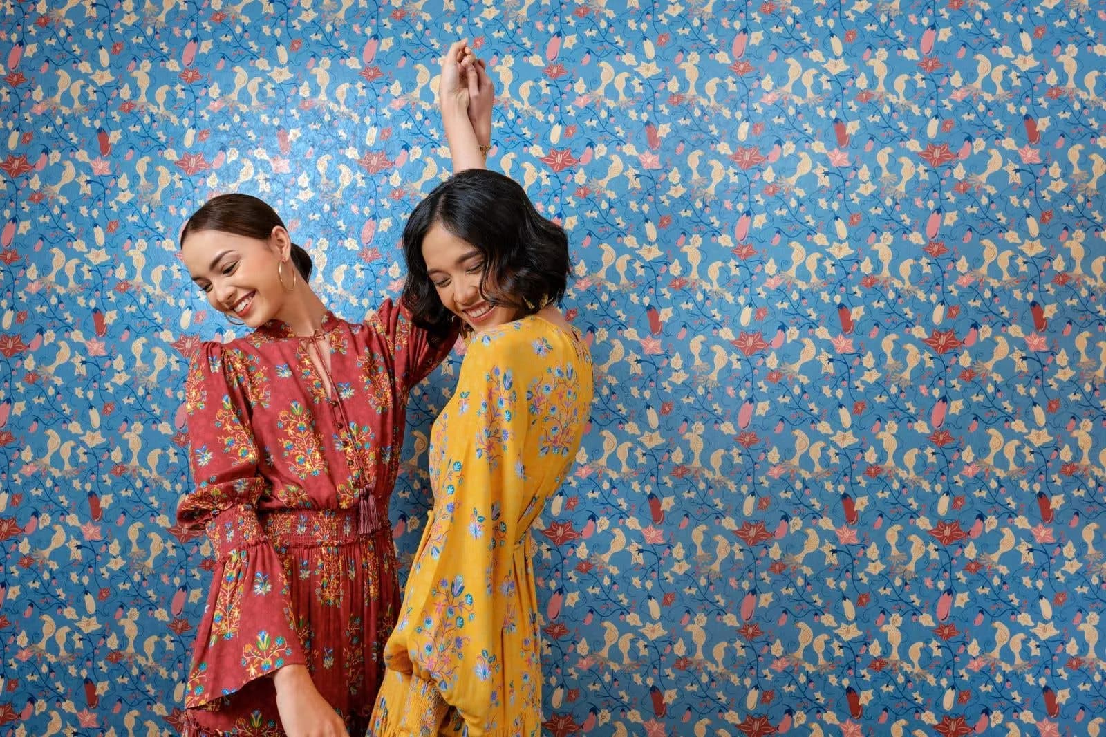 Two girls in floral long dresses joyfully dancing outdoors, spinning with laughter as their dresses flow in the breeze, set against a bright and sunny natural backdrop