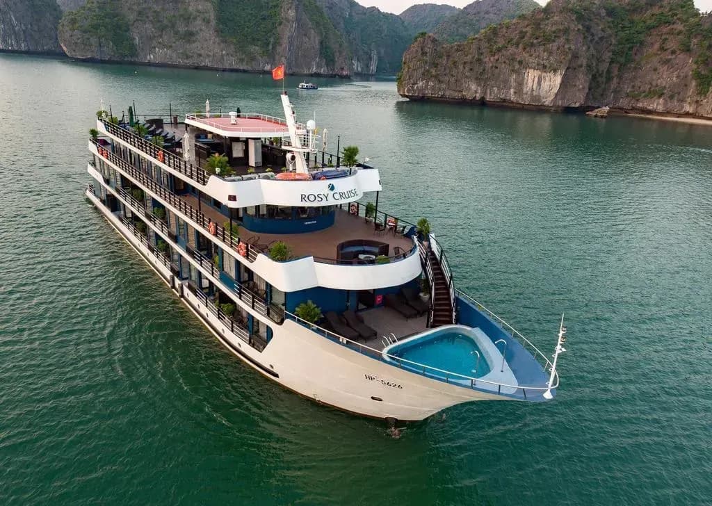 Image of a luxury yacht on a bay, with a small swimming pool in front and a limestone mountain backdrop behind.