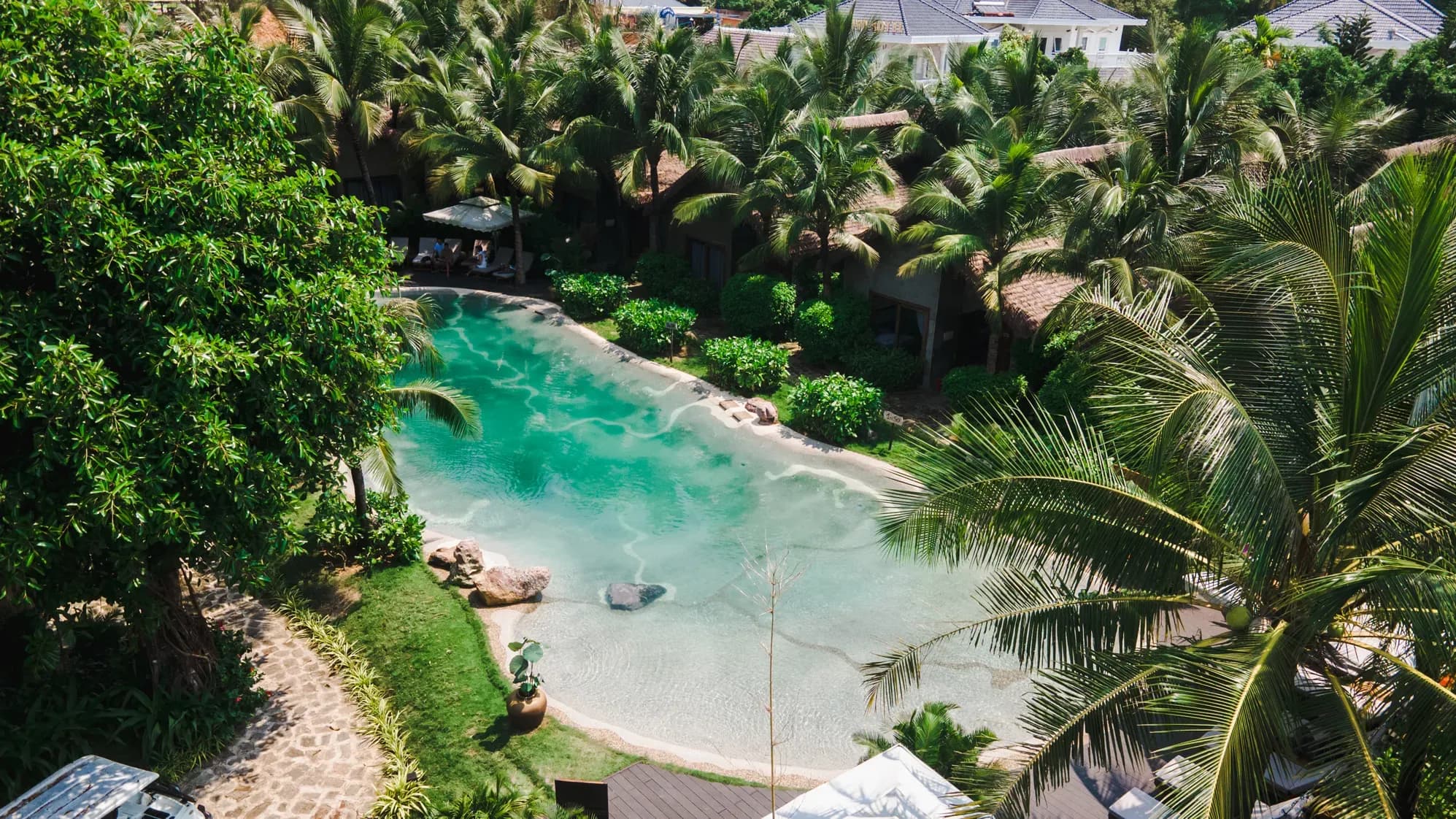 The photo captures a refreshing green swimming pool surrounded by lush trees, offering maximum relaxation for guests at M Village Phú Quốc.